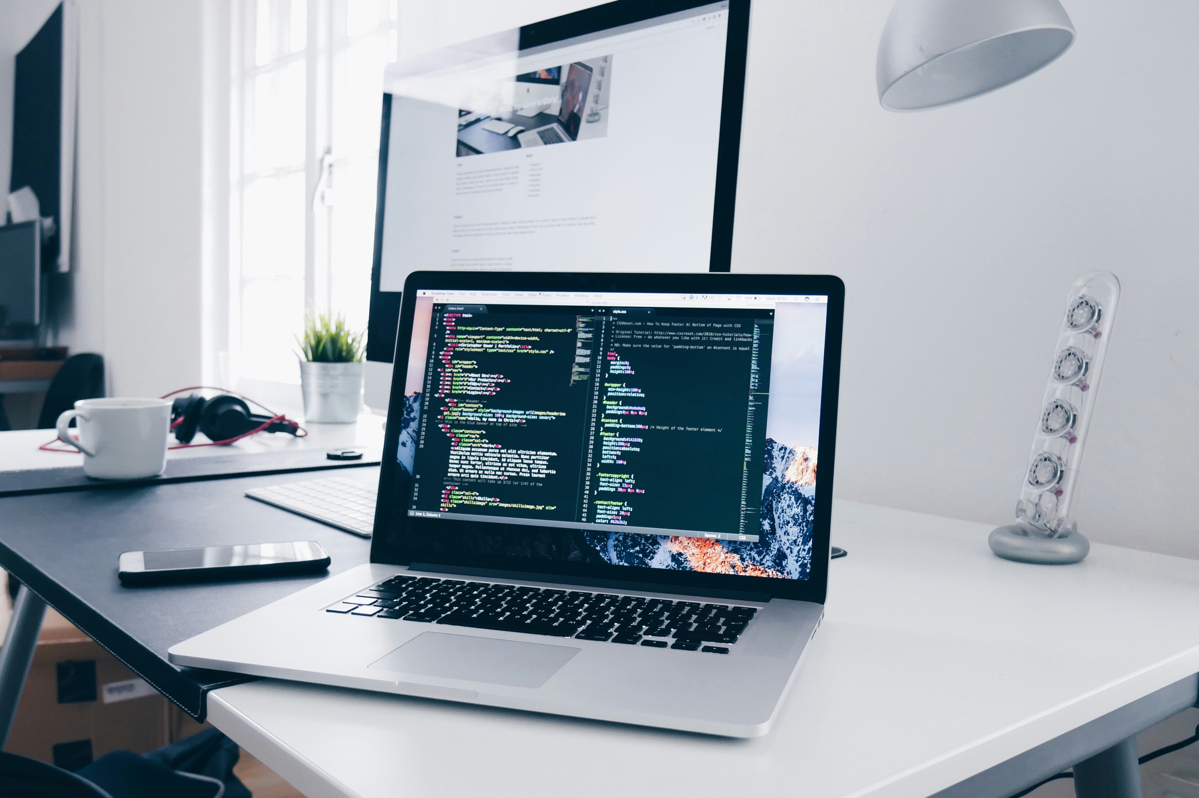 A MacBook With Lines of Code on it's Screen on a Busy Desk by Christopher Gower